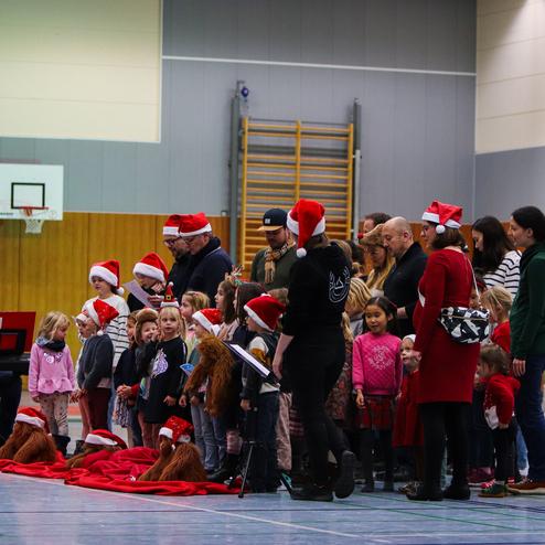 Weihnachtliche Veranstaltung mit Kindern und Erwachsenen in roten Nikolausmützen, singend vor einem Keyboardspieler.