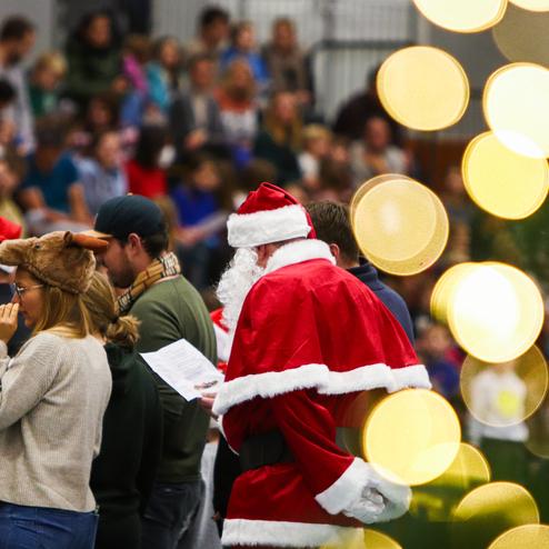 Auftritt einer Gruppe von Personen in Weihnachtskleidung, darunter ein Mann im roten Weihnachtsmannkostüm, in einer festlichen Halle.
