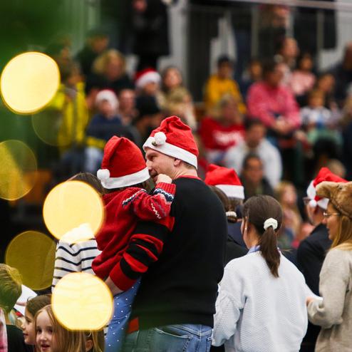 Familienmitglieder in Weihnachtsmützen stehen in einer geschäftigen Halle mit Zuschauer im Hintergrund.