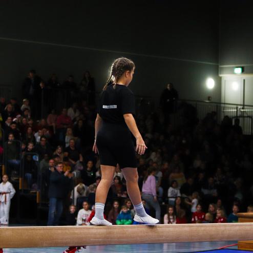 Mädchen balanciert auf einem Schwebebalken während einer Sportveranstaltung vor Publikum.