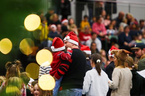 Familienmitglieder in Weihnachtsmützen stehen in einer geschäftigen Halle mit Zuschauer im Hintergrund.