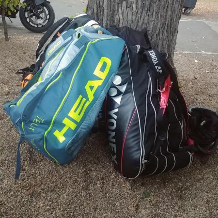 Zwei Sporttaschen, eine von Yonex und eine von Head, liegen auf einem kiesbedeckten Boden neben einem Baum.