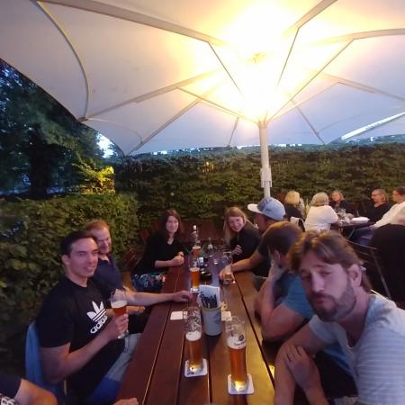 Gruppe von Personen sitzt unter einem großen Sonnenschirm an einem Tisch mit Getränken in einem Garten.