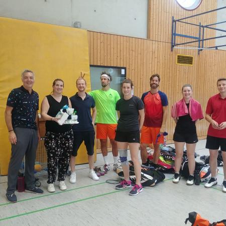 Gruppe von sieben Personen in Sportkleidung steht in einer Halle, einige halten Ausrüstung, lächeln und posieren für ein Foto.