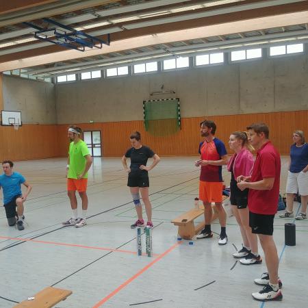 Gruppe von Sportlern in bunten Trikots, die in einer Sporthalle auf eine Trainingseinheit warten.