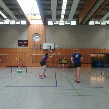 Badmintontraining in einer Sporthalle mit mehreren Spielern und Netzen, die verschiedenen Übungen durchführen.