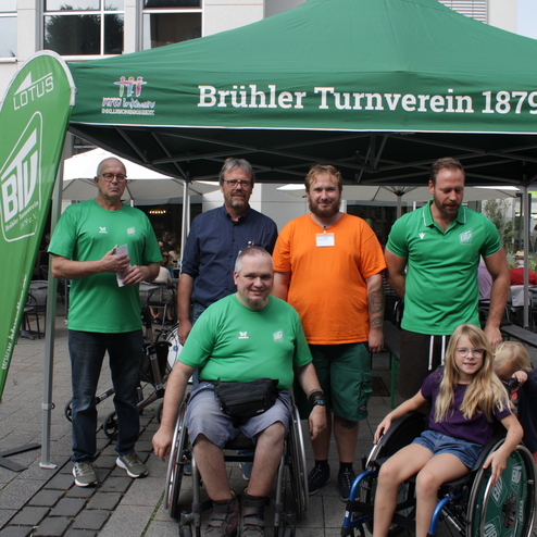 Gruppenfoto von Mitgliedern des Br&uuml;hler Turnvereins in gr&uuml;nen T-Shirts sowie einem Kind im Rollstuhl vor einem Zelt.