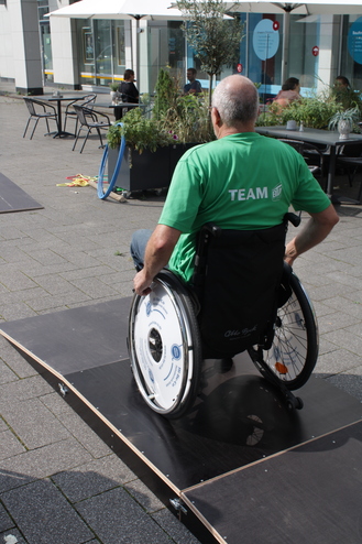 Mann im Rollstuhl fährt auf einer Rampe, umgeben von Pflanzen und Tischen in einem offenen Platz.