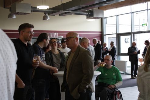 Menschen in einem modernen Raum unterhalten sich und trinken, einige stehen an Stehtischen, andere sitzen.