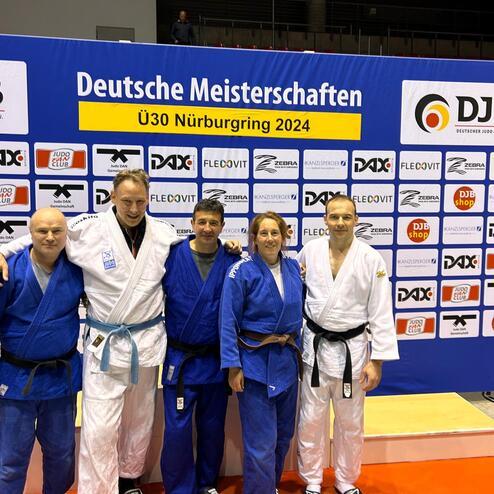 F&uuml;nf Judo-Athleten in Judogi posieren l&auml;chelnd vor einer Sponsorenwand bei den Deutschen Meisterschaften U30 2024.