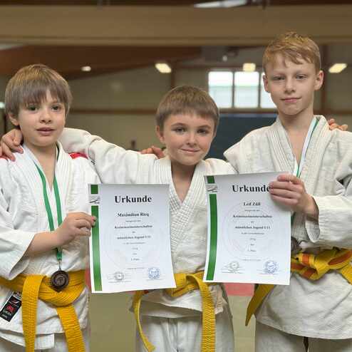 Drei Jungen in Judokleidung halten Urkunden für den 3. Platz bei einem Judoturnier. Im Hintergrund eine Judomatte.