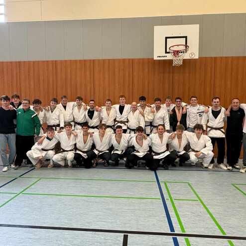 Gruppenfoto von 34 Judokas in wei&szlig;er und schwarzer Judogewandung in einer Sporthalle. Hintergrund mit Holzverkleidung.