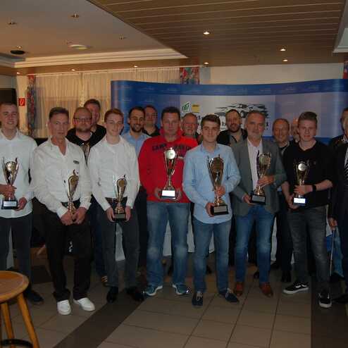 Gruppe von 14 Menschen in festlicher Kleidung, die Pokale in einem Restaurant nach einer Auszeichnung präsentieren.