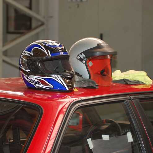 Zwei Motorradhelme, einer blau und schwarz, der andere grau mit rotem Innenteil, liegen auf einem roten Auto.