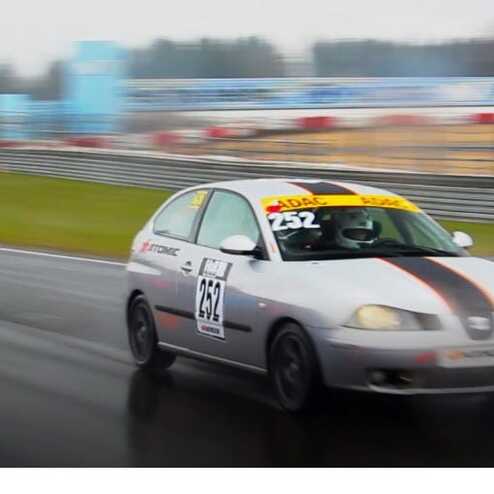 Zwei Rennwagen fahren bei Regen auf einer Rennstrecke, einer in Silber und der andere in Orange.