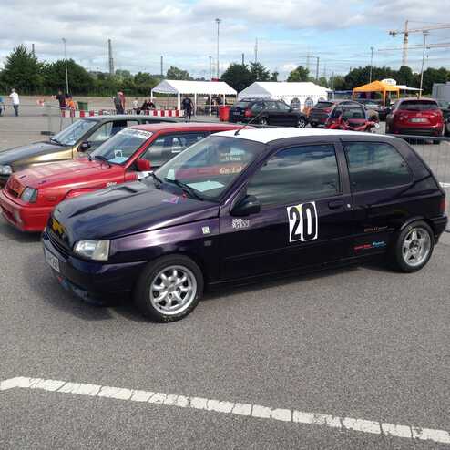 Vier farbige Kleinwagen stehen auf einem Parkplatz, im Hintergrund sind Fahrzeuge und Zelte zu sehen.