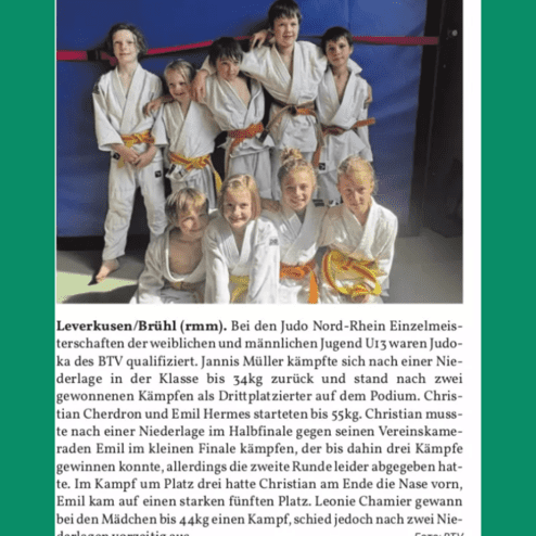 Gruppe von Judokas in weißen und farbigen Anzügen posiert lächelnd auf einer Matte, hinter ihnen ein blauer Hintergrund.