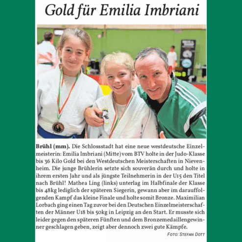 Zwei junge Judokas mit Medaillen stehen lächelnd mit einem Trainer in einem Sportzentrum. Hintergrund ist eine grüne Wand.