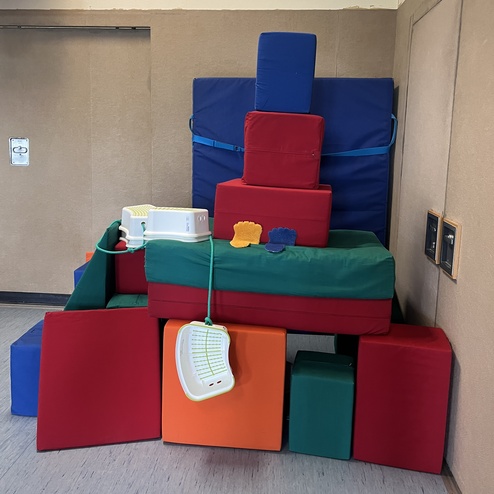 Bunte Kletter- und Spielkonstruktion aus gepolsterten Blöcken in einem Raum mit Holzfußboden.