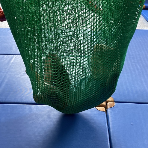 Grüne Netzhaube hängt über blauer Gymnastikmatte, mit einem Teil des Inhalts sichtbar darunter.