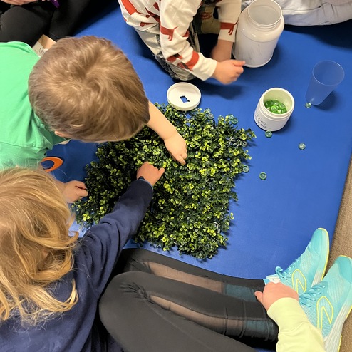 Kinder sammeln grüne Perlen auf einer blauen Matte, umgeben von Behältern. Ein kreatives Bastelprojekt in Aktion.
