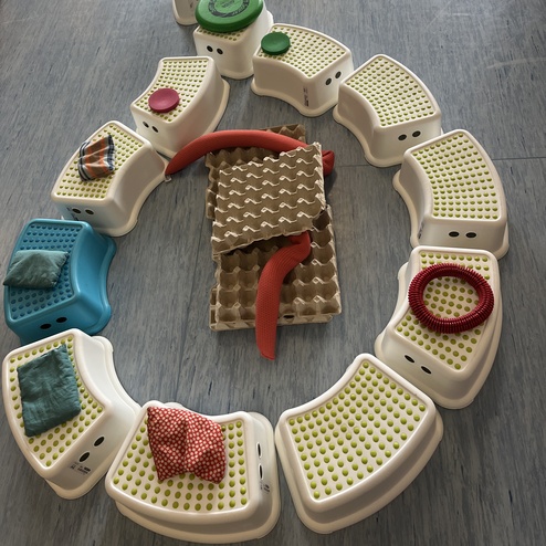 Bunte Sitzmodule und verschiedene Texturen bilden eine geschwungene Strecke auf einem Bodenbelag.