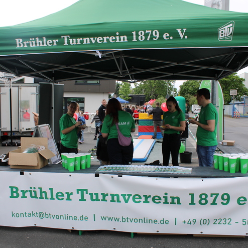 Stand des Br&uuml;hler Turnvereins 1879 e.V. mit Mitarbeitern in gr&uuml;nen T-Shirts, Tischen und Veranstaltungen im Hintergrund.