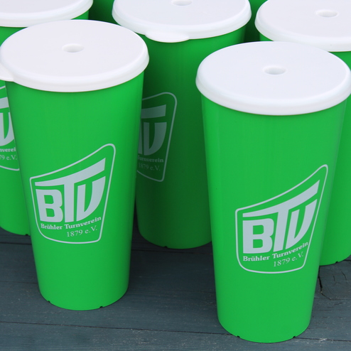 Gr&uuml;ne Kunststoffbecher mit wei&szlig;em Deckel und dem Logo des Br&uuml;hler Turnvereins 1879 e.V. in der N&auml;he von Holzoberfl&auml;che.