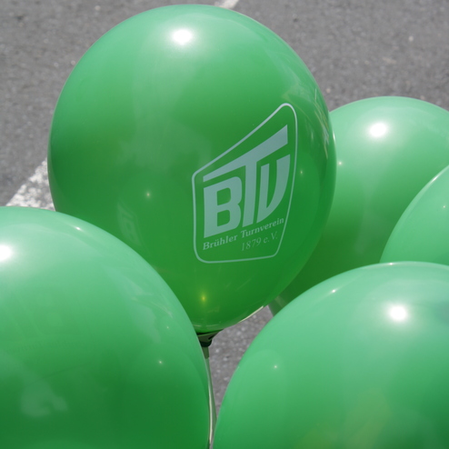 Gr&uuml;ne Ballons mit dem Logo des Br&uuml;hler Turnervereins 1879 e.V. auf einem Asphaltboden.