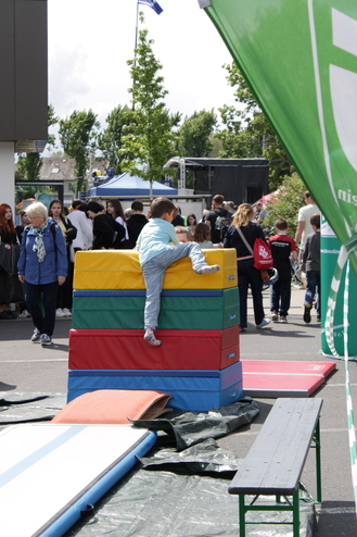 Ein Kind klettert auf einen bunten Schaumstoffblockstapel, während Besucher eines Festes im Hintergrund laufen.