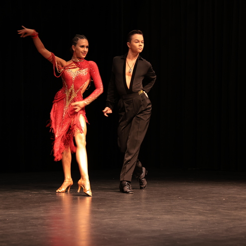 Tanzpaar in farbenfrohen Kost&uuml;men f&uuml;hrt einen lebhaften Tanz auf einer B&uuml;hne mit schwarzem Hintergrund auf.