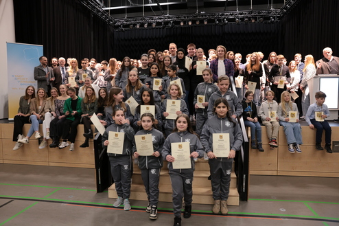 Gruppenfoto bei einer Preisverleihung mit jungen Sportlern, die Urkunden in der Hand halten, auf einer Bühne.
