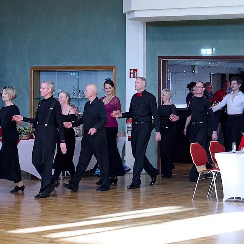 Tanzende Paare in eleganter Kleidung betreten einen festlich dekorierten Saal.