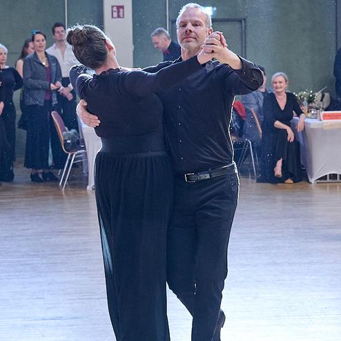 Tanzpaar in eleganter Kleidung tanzt in einer festlichen Umgebung, im Hintergrund Zuschauer auf einer Tanzveranstaltung.