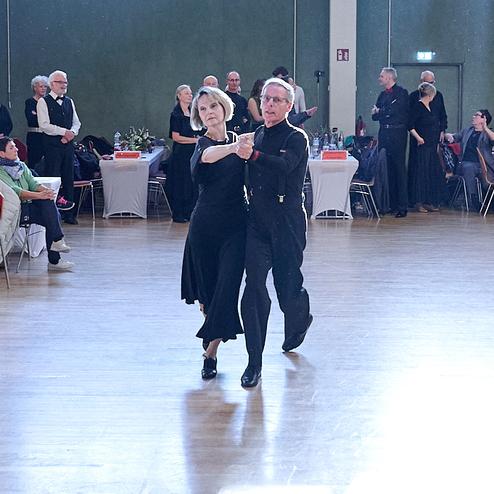 Tanzpaar in eleganter Kleidung führt einen klassischen Tanz auf einer beleuchteten Tanzfläche in einem Saal aus.