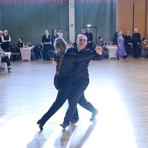 Tanzendes Paar in blauen Outfits auf einer Tanzfläche, umgeben von Publikum in einem festlichen Saal.