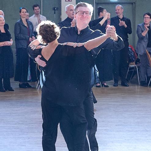 Tanzpaar in eleganter Kleidung während eines Tanzwettbewerbs, umgeben von applaudierendem Publikum.