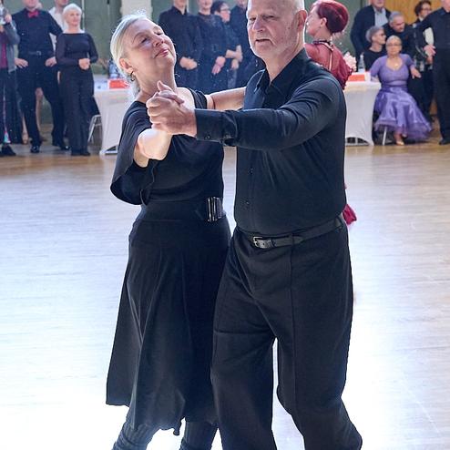 Tanzendes Paar in schwarzer Kleidung auf einer Tanzfläche, umgeben von einer Zuschauermenge.