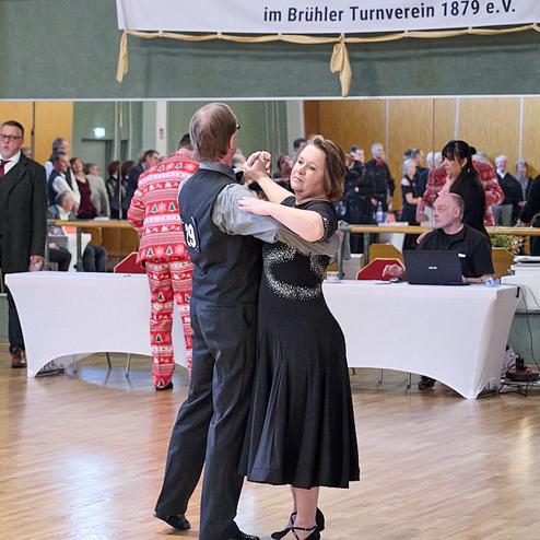 Tanzpaar in eleganter Kleidung tanzt auf einer Sportveranstaltung, im Hintergrund Zuschauer und ein Banner des TSC Brühl.