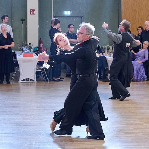 Tanzpaar in eleganter Kleidung führt einen Walzer auf einer Tanzfläche vor Publikum aus.