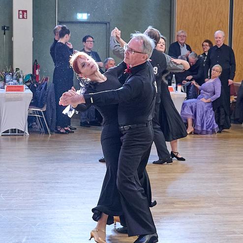 Tanzpaar in eleganter Kleidung führt einen Tanzschritt auf einer Holztanzfläche während einer Veranstaltung.