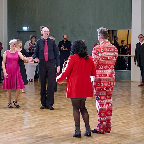Tanzveranstaltung in einem Saal mit mehreren Teilnehmern, die in festlicher Kleidung miteinander tanzen.