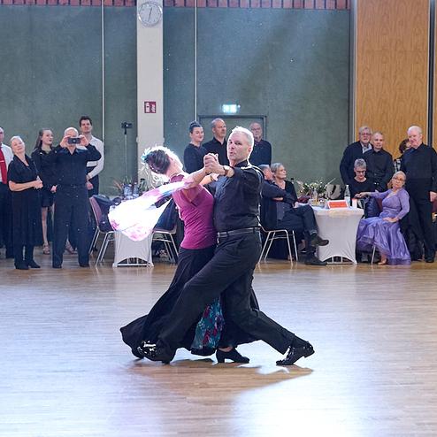 Tanzpaar in eleganter Kleidung führt eine anspruchsvolle Choreografie auf einer Tanzfläche vor Publikum auf.