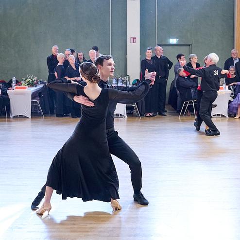 Tanzpaar in eleganter Kleidung führt einen Ausdruckstanz auf, Zuschauer im Hintergrund applaudieren.