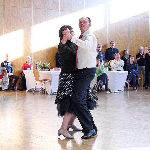 Tanzendes Paar in eleganter Kleidung auf einer hellen Tanzfläche, Zuschauer verfolgen aufmerksam.