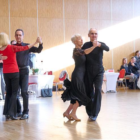 Tanzende Paare in eleganter Kleidung auf einer festlichen Tanzveranstaltung in einem hellen Saal.