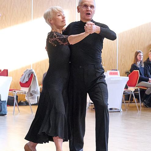 Tanzpaar in eleganter Kleidung führt einen Paartanz auf einer Holzfußbodenfläche in einem hellen Raum aus.