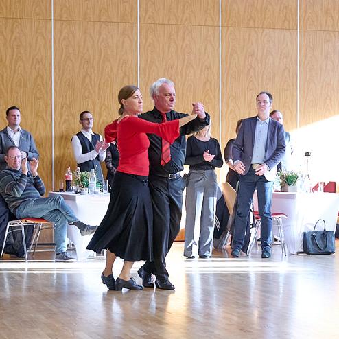 Tanzendes Paar in eleganter Kleidung, umgeben von applaudierenden Gästen in einem festlichen Saal.