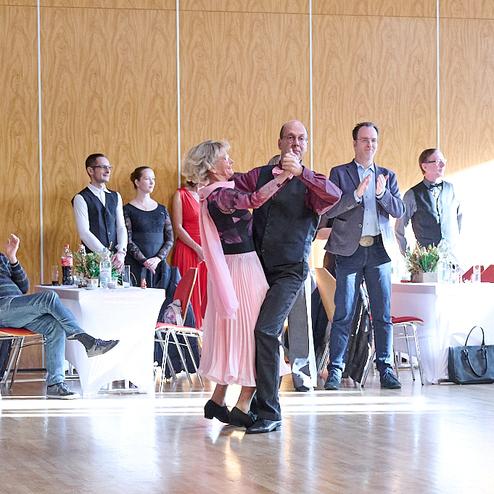 Tanzpaar in festlicher Kleidung führt einen Tanz auf einer Veranstaltung vor Zuschauern vor.