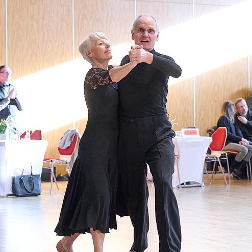 Älteres Paar tanzt miteinander in eleganter Kleidung auf einer lichtdurchfluteten Tanzfläche.